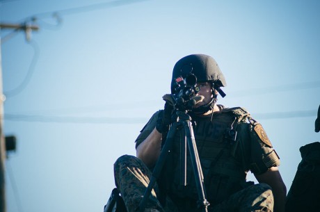 Police sharpshooter with weapon trained in the direction of the camera at protests in Ferguson - Photo by Jamelle Bouie